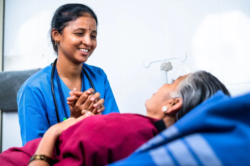 A nurse holding an older patient's hand and offering reassurance at the bedside