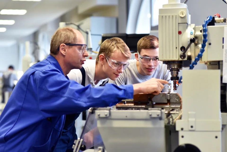 An instructor guiding apprentices at a machine in a technical workshop